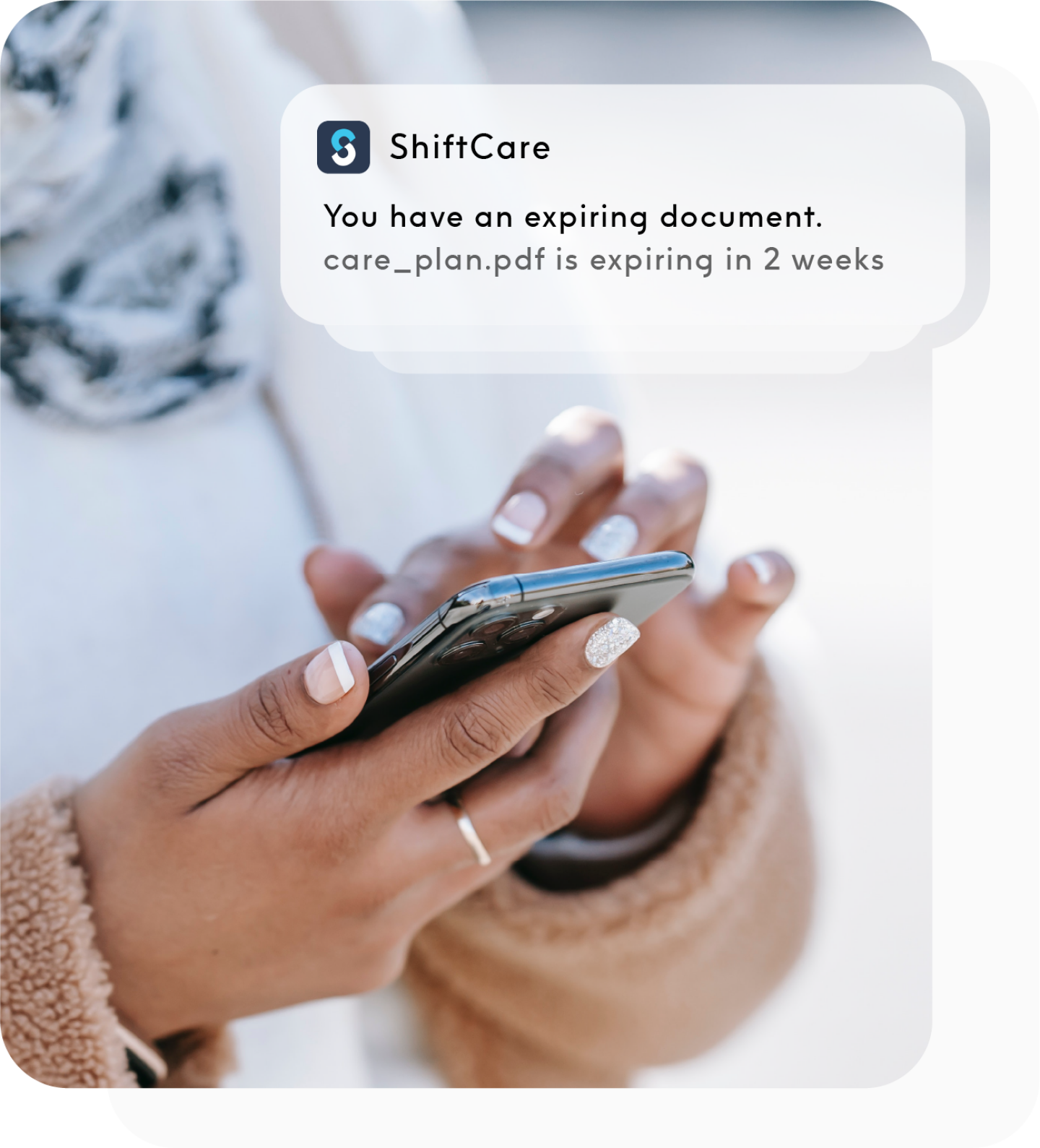 Worker holding phone, getting a ShiftCare mobile app notification for a client document expiring in 2 weeks
